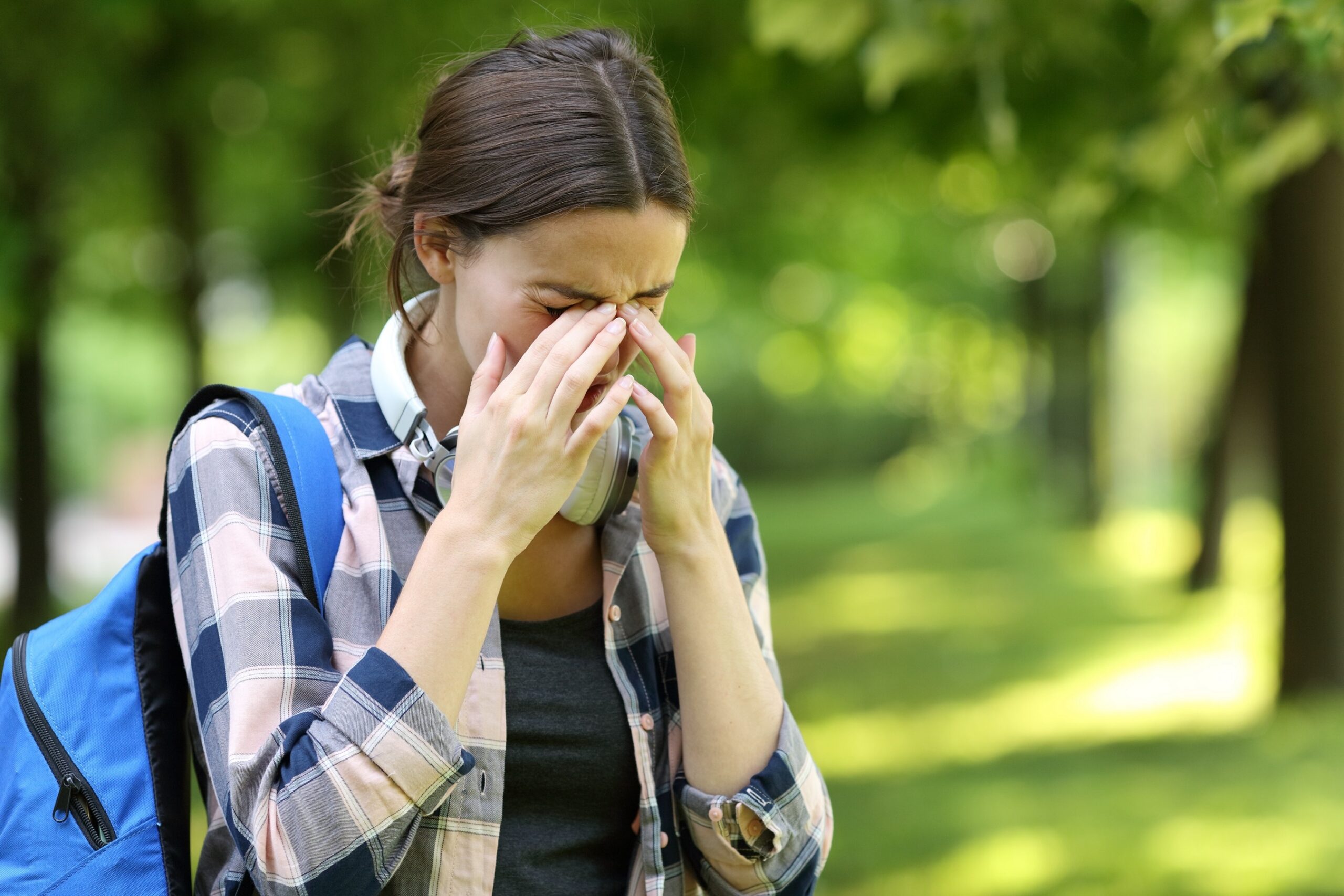 Young woman rubbing itchy eyes outdoors during allergy season