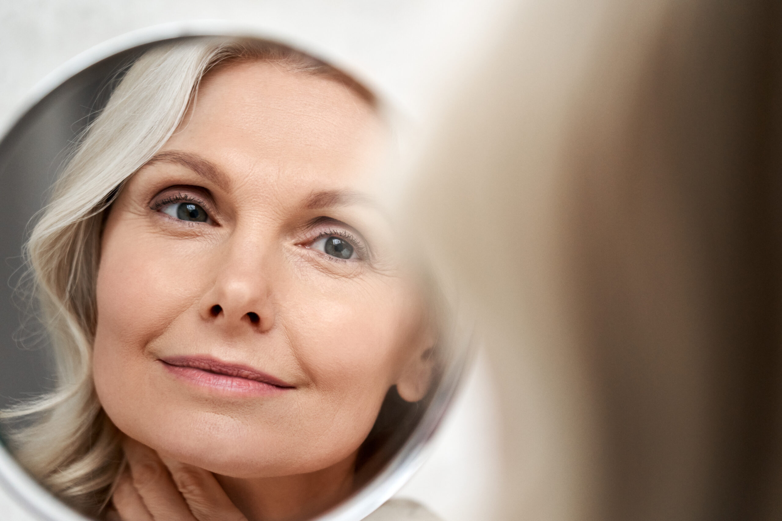 Smiling woman touching her face while looking in a mirror