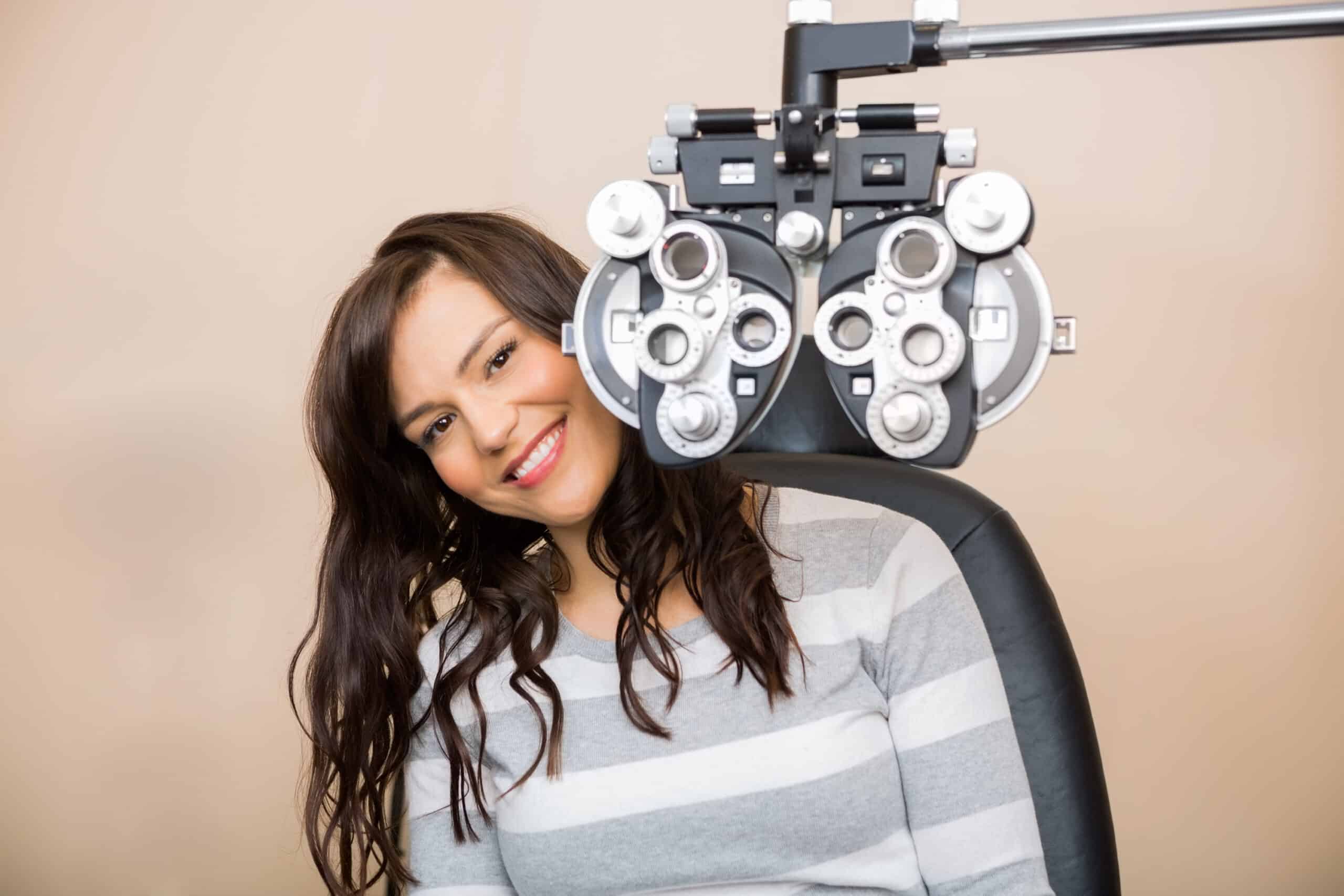 Happy young woman sitting behind a phoropter during an eye exam